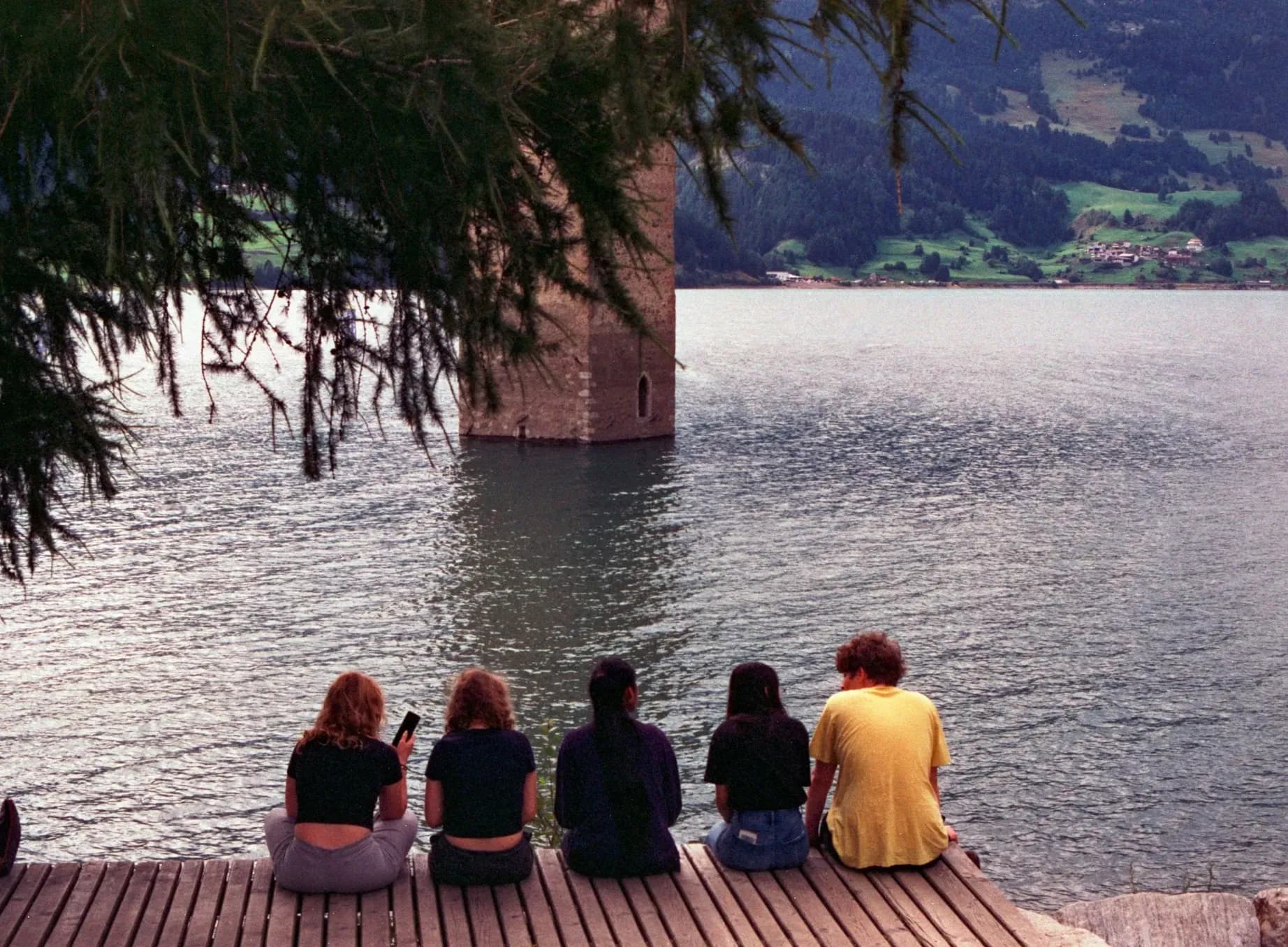 Cinq femmes assises sur un ponton face au lac de Resia et au clocher immergé de Graun, Tyrol du Sud