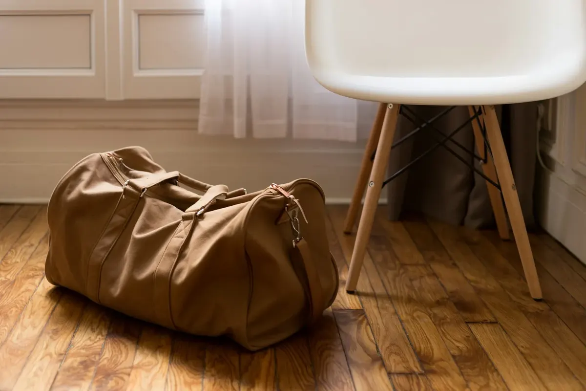 Reisetasche aus Leder auf einem Holzboden neben einem weißen Stuhl