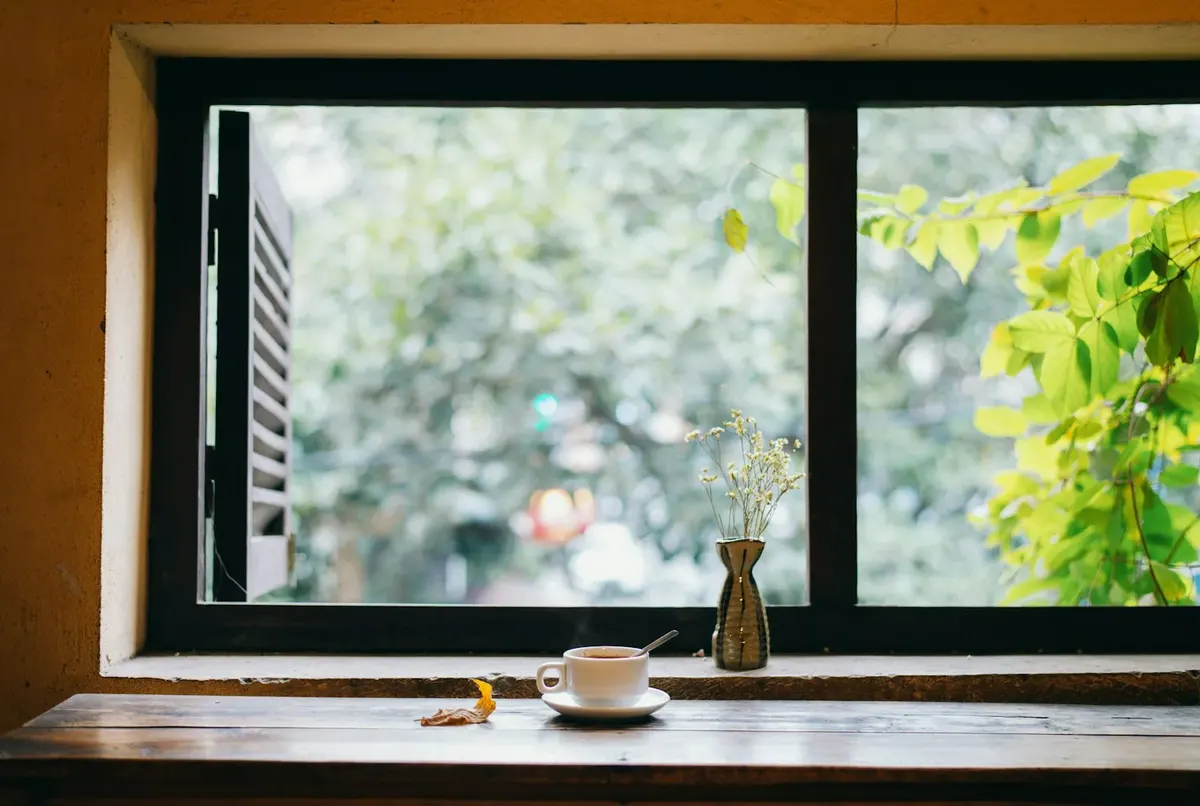 Tasse und kleine Vase auf einem Fensterbrett mit Blick ins Grüne